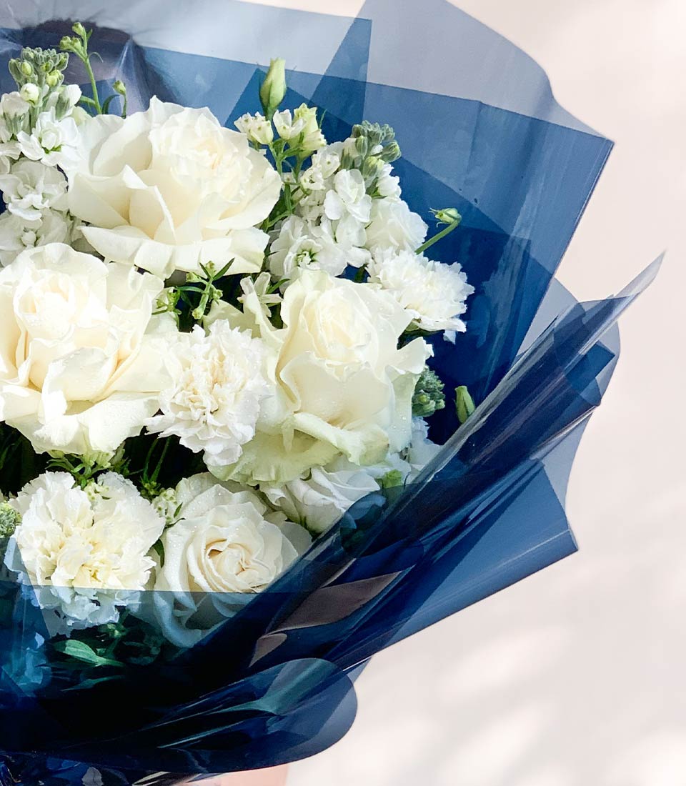 Fresh white roses and carnations bouquet wrapped in blue cellophane, premium gift flowers