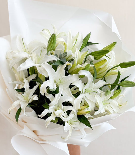 Premium white lily bouquet with yellow centers, lush green foliage, wrapped in elegant white paper
