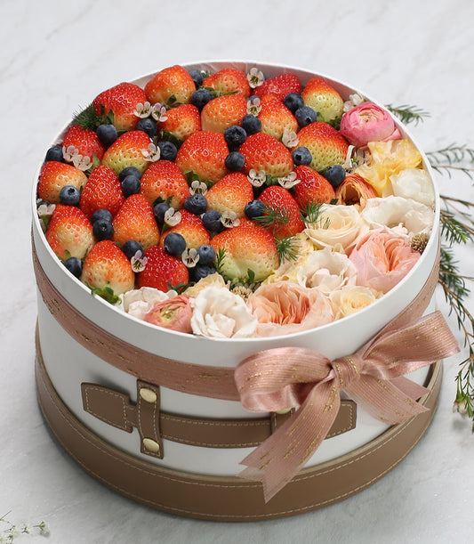 Luxury white hatbox with fresh strawberries, blueberries, and mixed garden flowers in peach and pink tones, birthday gift