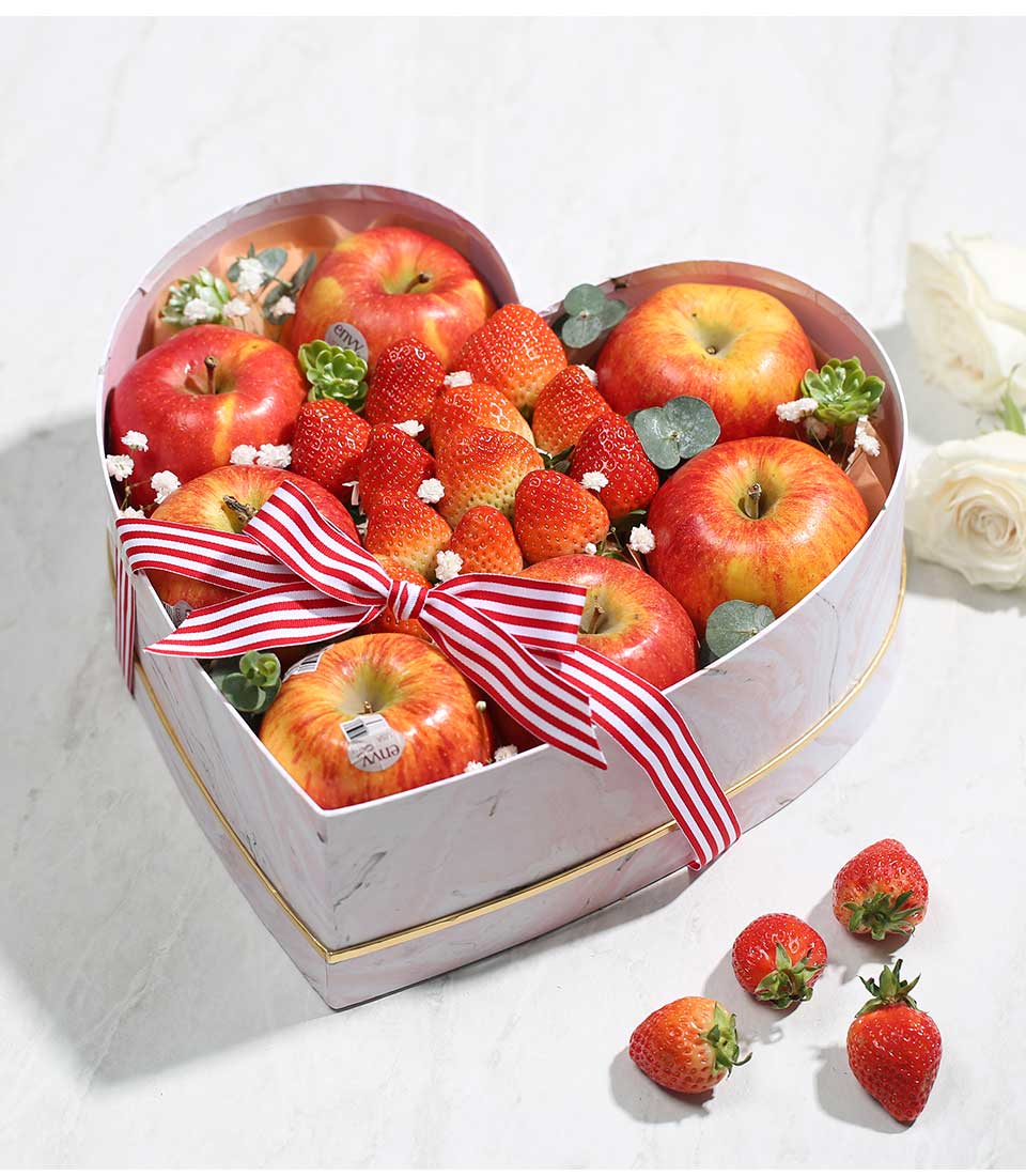 Heart-shaped white marble fruit box with fresh red apples and strawberries, tied with red striped ribbon for birthdays