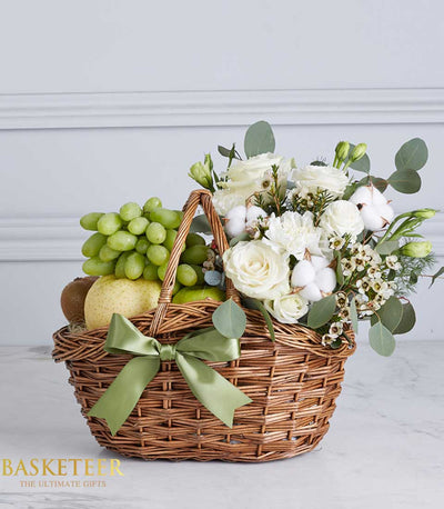 Rustic wicker basket with fresh green grapes, pear, kiwi, apples and white roses with eucalyptus, tied with light green