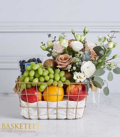 Premium fruit and flower gift basket with green grapes, berries, kiwi, apples, and white-pink floral arrangement in gold
