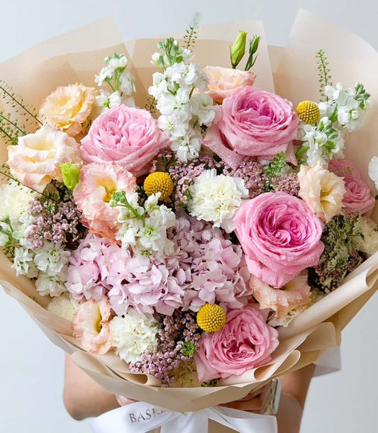 Vibrant mixed flower bouquet with pink garden roses, white stock, hydrangeas, and yellow craspedia in kraft paper wrap