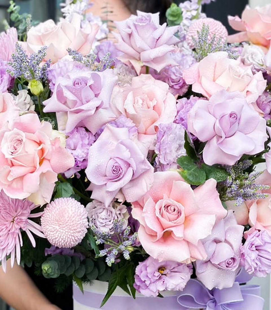 Pink and lavender rose bouquet with purple blooms in white striped hatbox, fresh celebration flowers