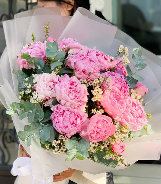 Lush pink peony bouquet with eucalyptus and white filler flowers, wrapped in tissue and white ribbon
