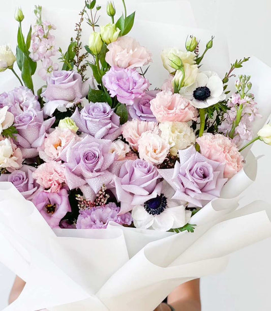 Purple and pink pastel rose bouquet with lisianthus and anemones, white paper wrapped