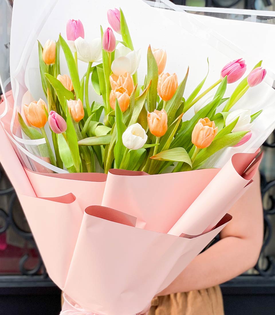 Spring tulip bouquet in pink, white, and orange with fresh water droplets, wrapped in light pink paper