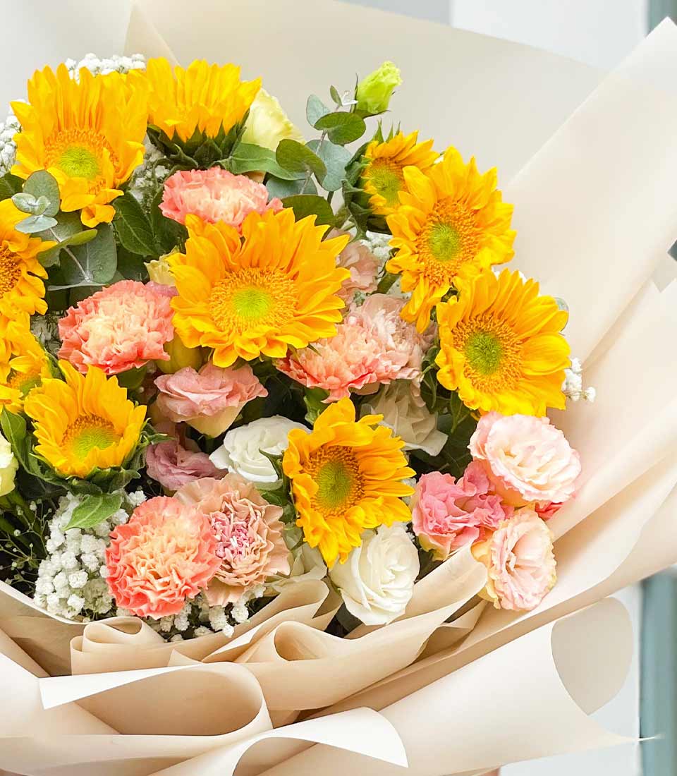 Bright yellow sunflowers with pink carnations and white roses in cream paper wrap, birthday gift bouquet