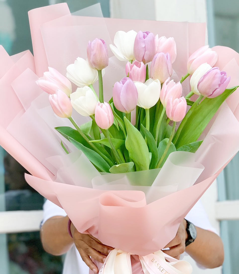 Blushing pink and purple tulip bouquet wrapped in layered paper with cream ribbon bow