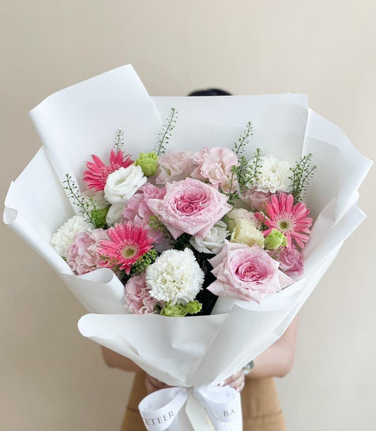 Fresh pink roses, carnations, and gerberas arranged with white eustoma in elegant white paper wrapping