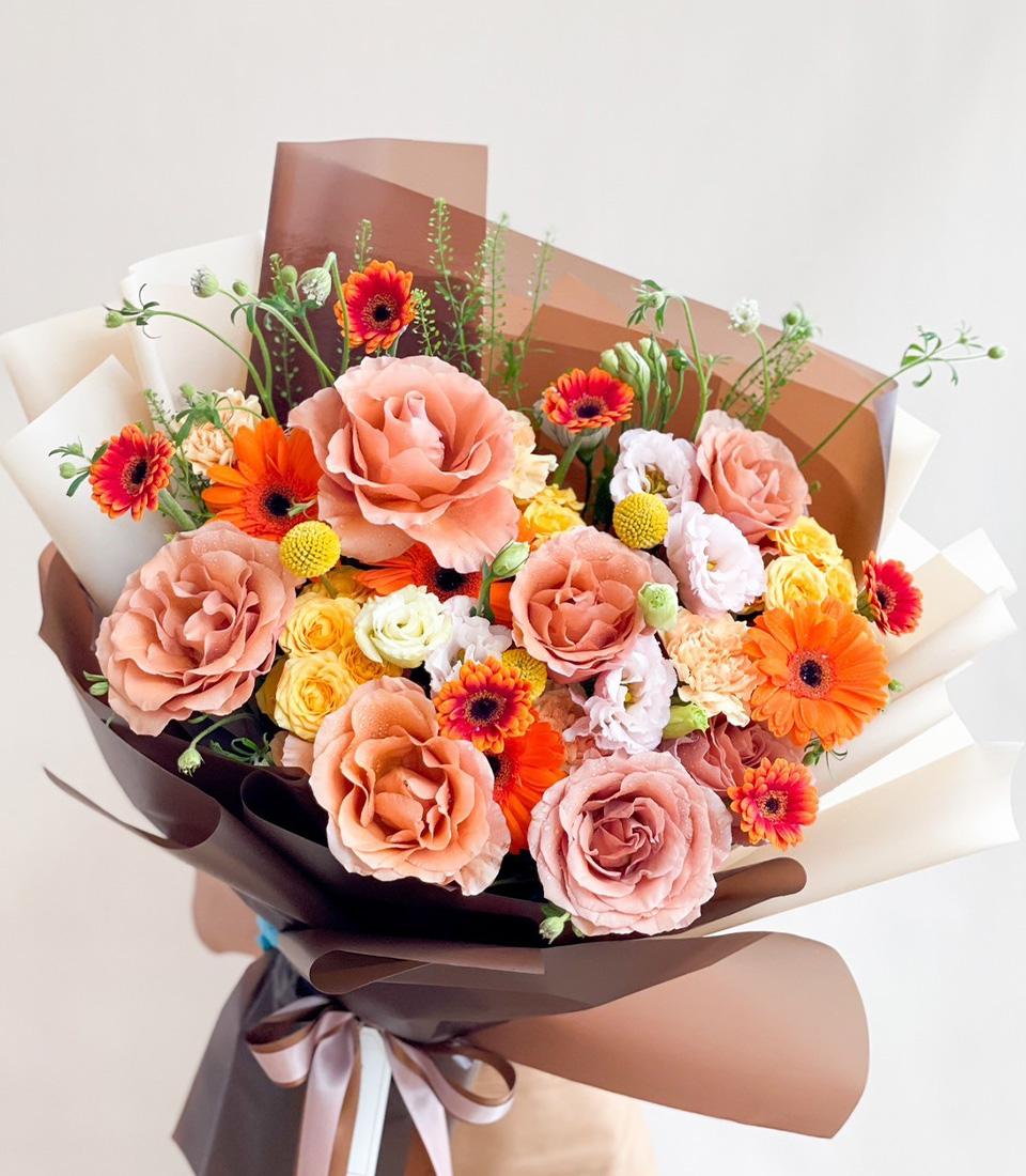 Sunset-hued bouquet with peach roses, coral gerberas, and yellow billy balls in luxe brown wrap