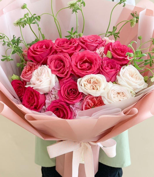 Pink and white rose bouquet with hydrangeas and green foliage, wrapped in pink paper with striped ribbon