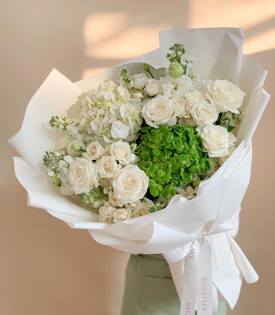 Elegant white rose and hydrangea bouquet with green accents, wrapped in crisp white paper