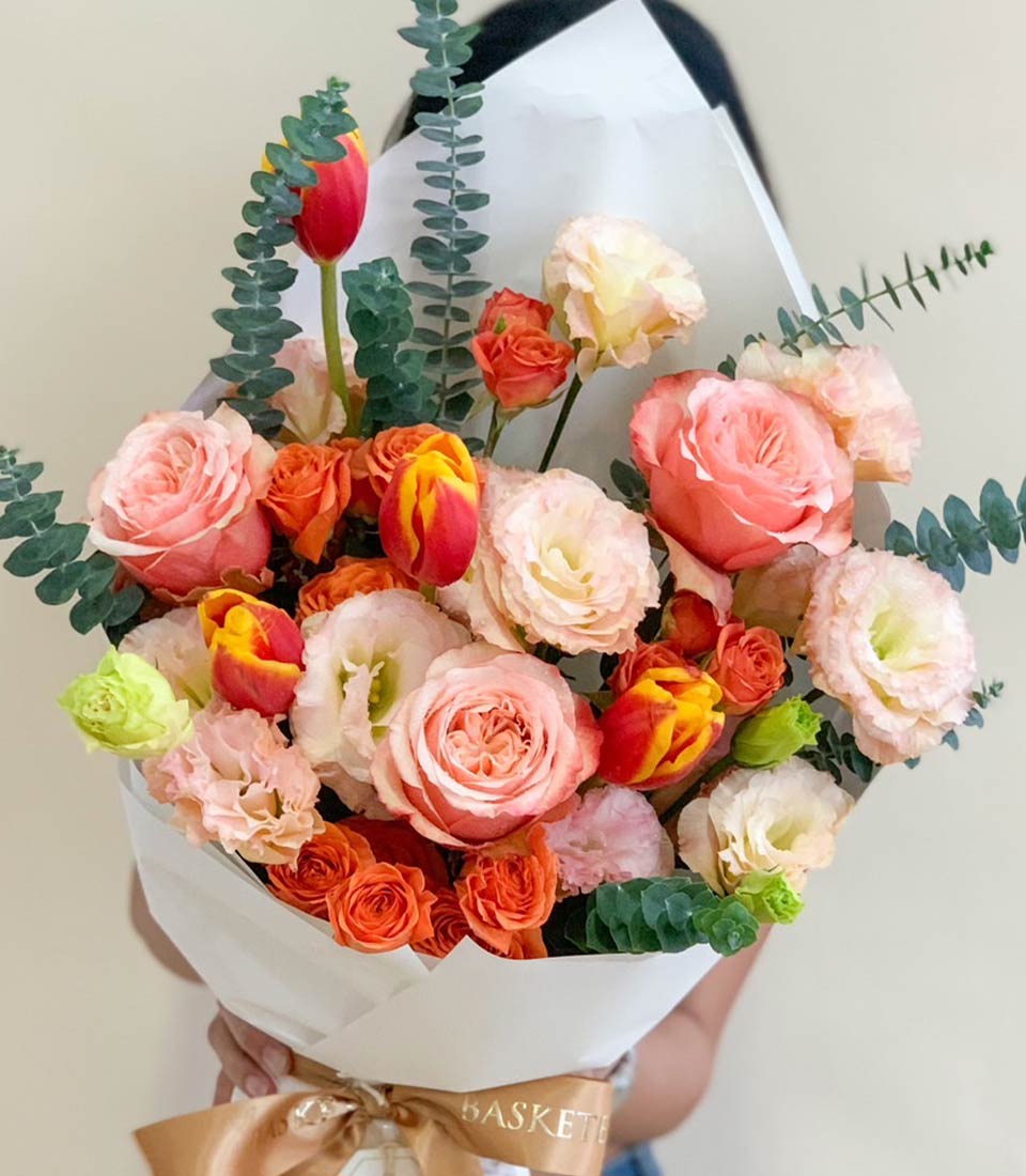 Vibrant mixed roses, tulips, and lisianthus bouquet in pink, orange, and yellow with eucalyptus