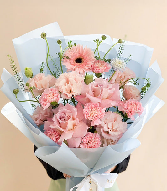 Blush pink roses and gerbera daisy bouquet with carnations, wrapped in light blue paper