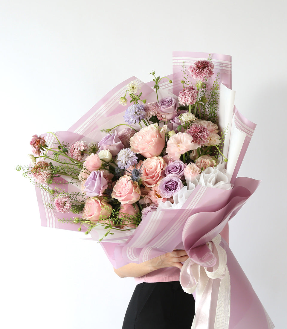 Lavish pink and purple rose bouquet with carnations, wrapped in striped paper and pink ribbon