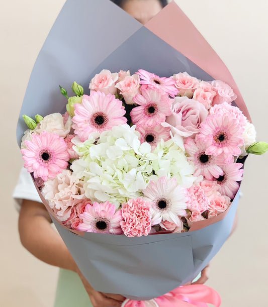 Large bouquet of pink gerberas, white hydrangeas, and spray roses wrapped in pastel blue and pink paper with bright pink