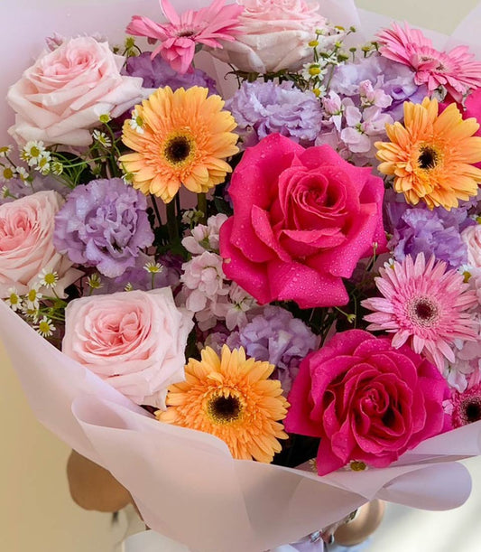 Vibrant mixed fresh flower bouquet with pink roses, orange gerberas, and purple filler flowers, wrapped in blush paper