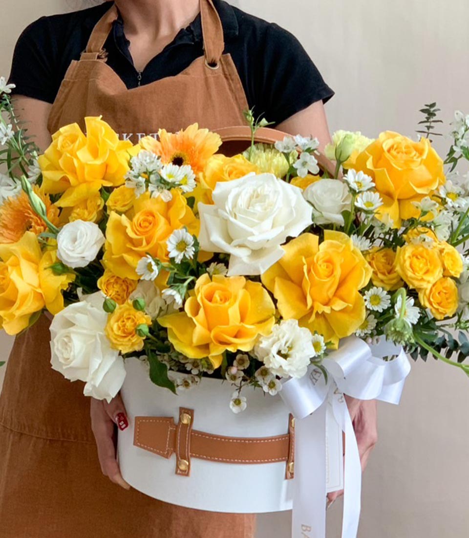 Cheerful spring flower arrangement with yellow and white roses, orange gerberas in luxury white box with leather strap