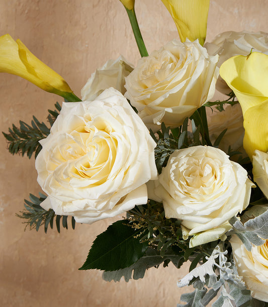 Creamy white roses and yellow calla lilies in a lush garden arrangement with dusty miller foliage