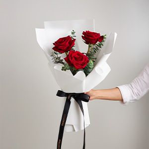 Three deep red roses with eucalyptus in white paper, tied with black ribbon