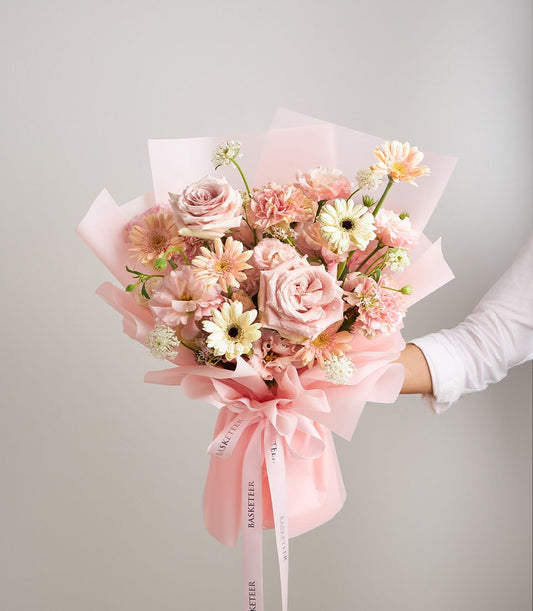 Romantic blush mixed bouquet of fresh roses, carnations, and gerbera daisies in pink and cream tones, hand-held with pink