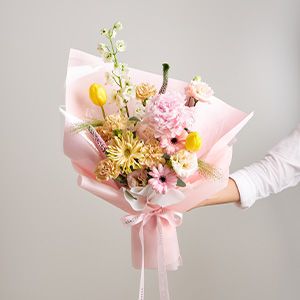 Pastel Joy bouquet with pink peonies, yellow tulips, and white delphiniums wrapped in light pink paper