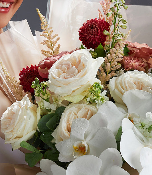 Premium rose and orchid bouquet with white roses, red chrysanthemums, and fresh tropical blooms wrapped in cream cellophane
