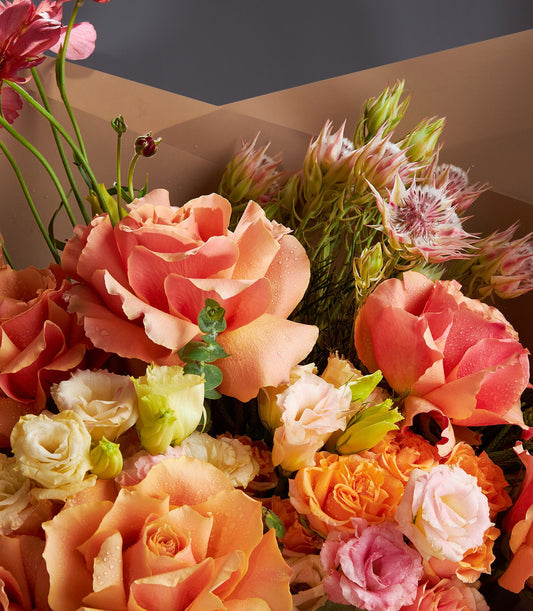 Sunset orange and peach roses with cream ranunculus in brown paper wrap