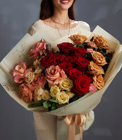 Large fresh rose bouquet in red, peach, and yellow with carnations, creamy paper wrap and satin ribbon