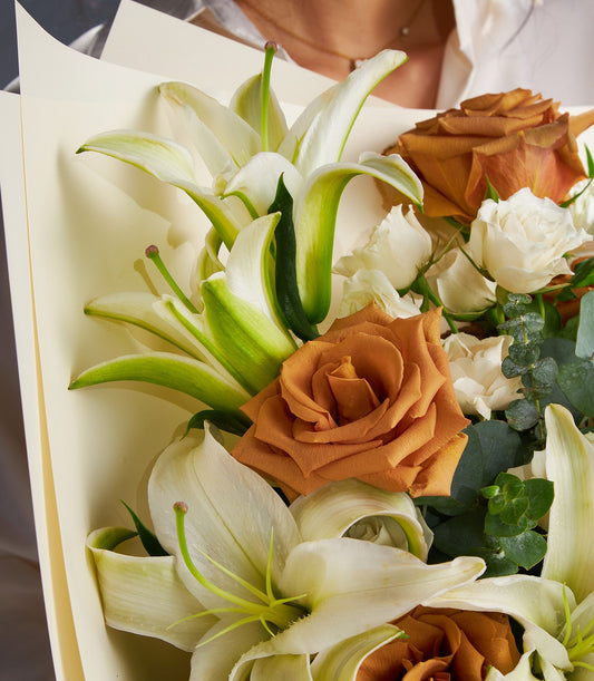 Premium white lily and burnt orange rose bouquet with eucalyptus, cream-wrapped luxury flower gift