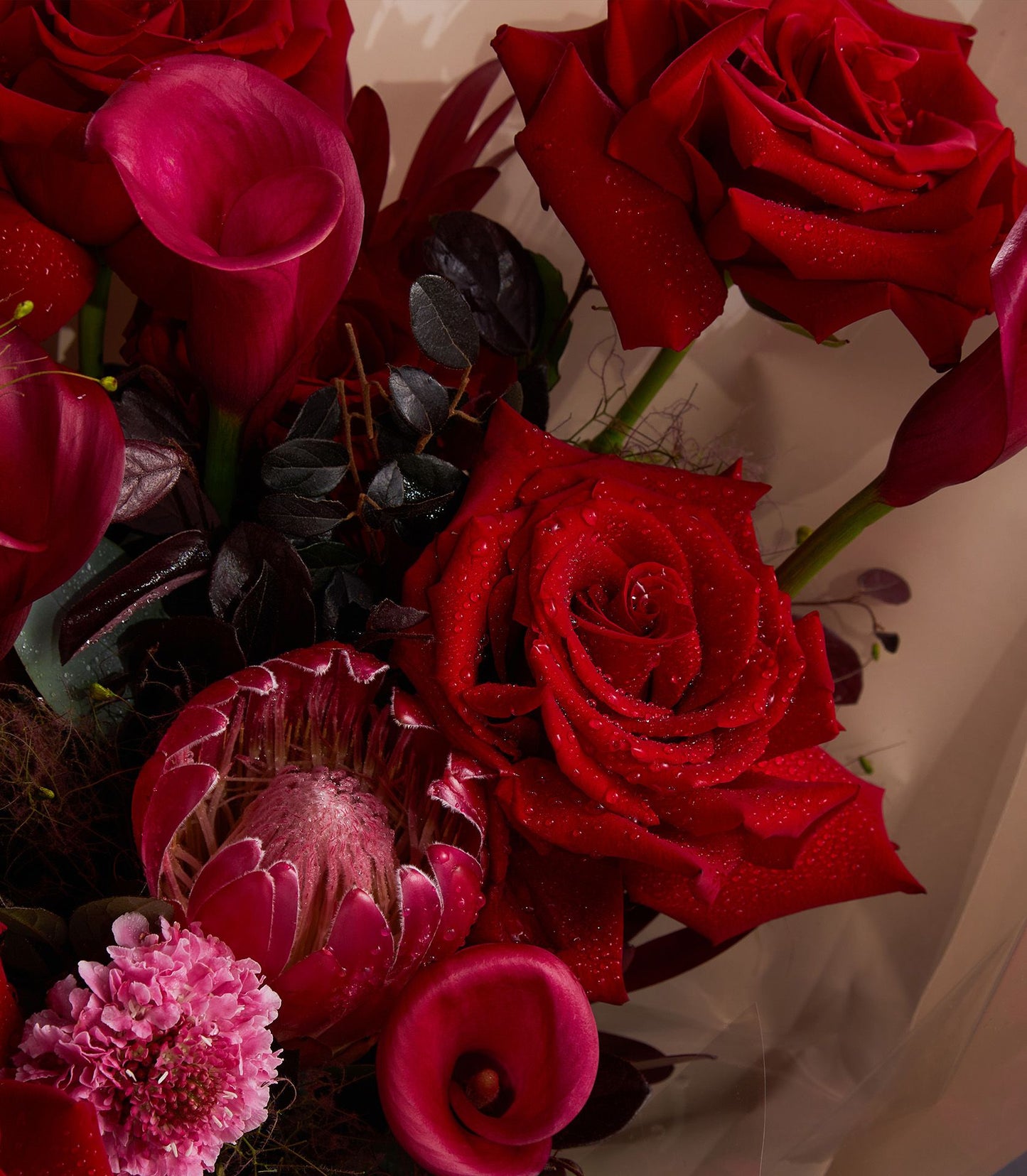 Deep red roses and fuchsia calla lilies with fresh water droplets in a premium gift bouquet