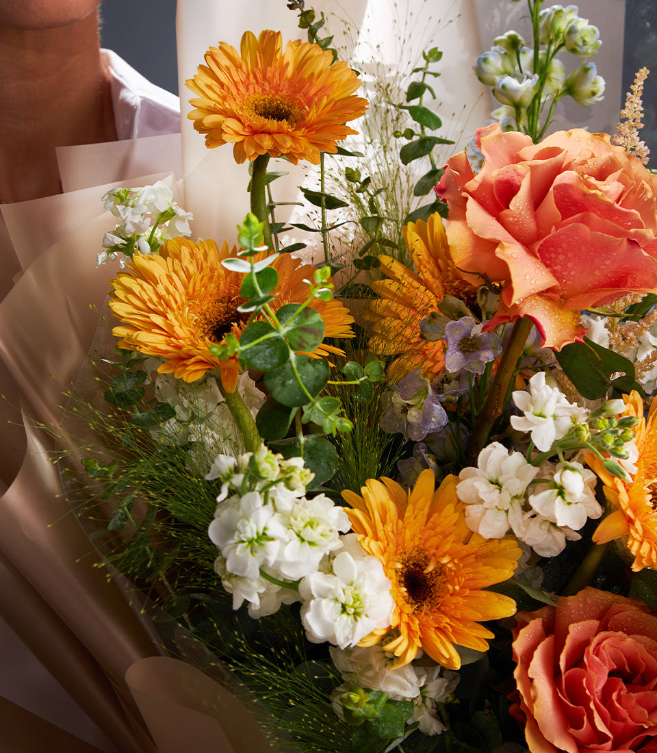 Vibrant fresh flower bouquet with orange gerberas, coral rose, and white blooms wrapped in kraft paper
