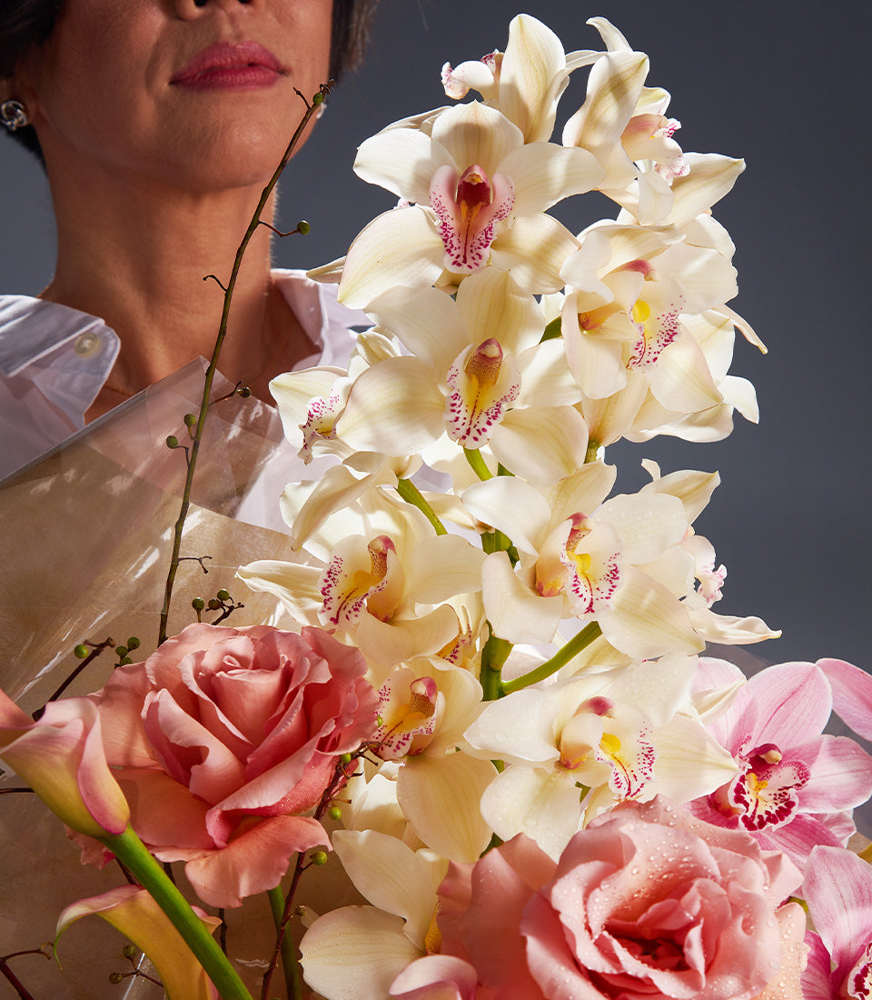 Elegant white and pink orchid and rose bouquet with water droplets wrapped in cellophane