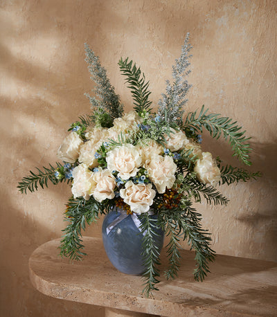 Cream and blue carnation arrangement in grey glass vase with fern foliage and berries