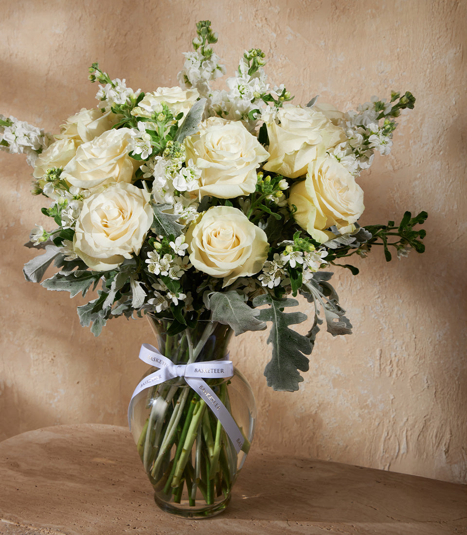 Cream and white roses in clear glass vase with ivory ribbon bow