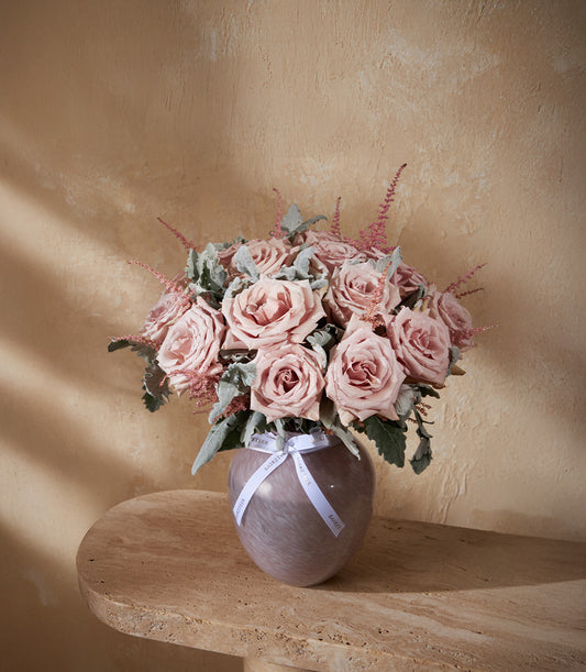 Dusty pink roses and astilbe in marbled purple-grey glass vase with silvery foliage and white ribbon