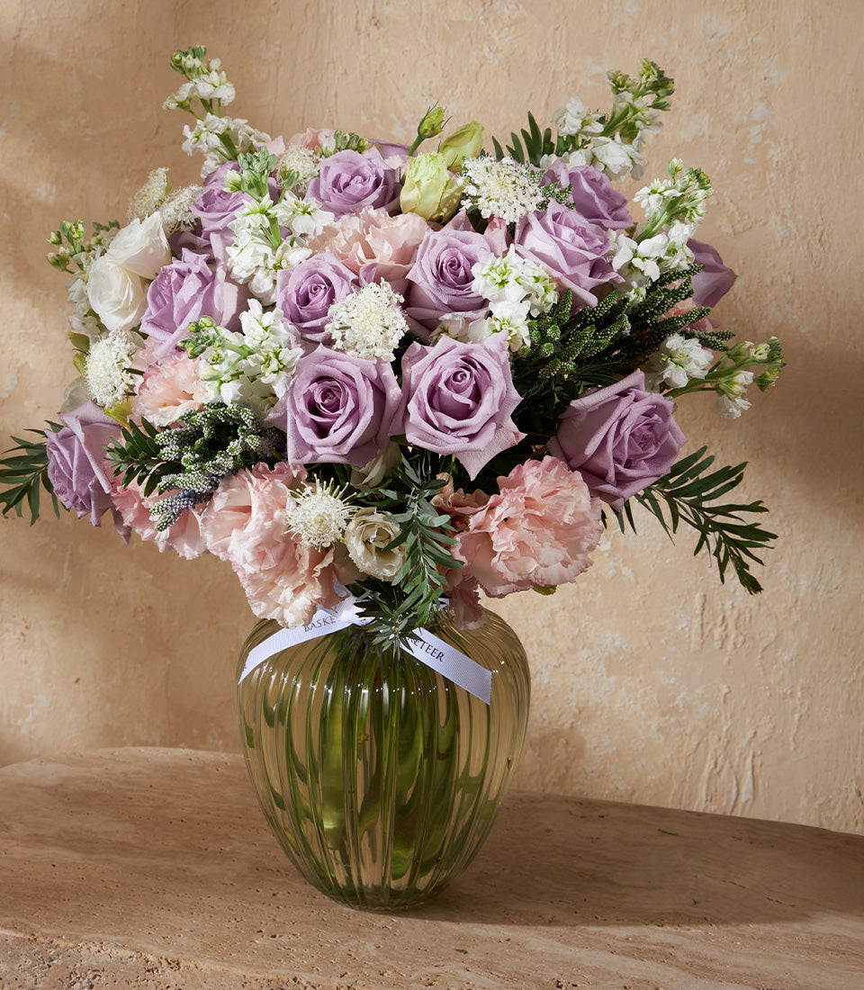 Lavender roses and pink carnations in ribbed green glass vase with white ribbon
