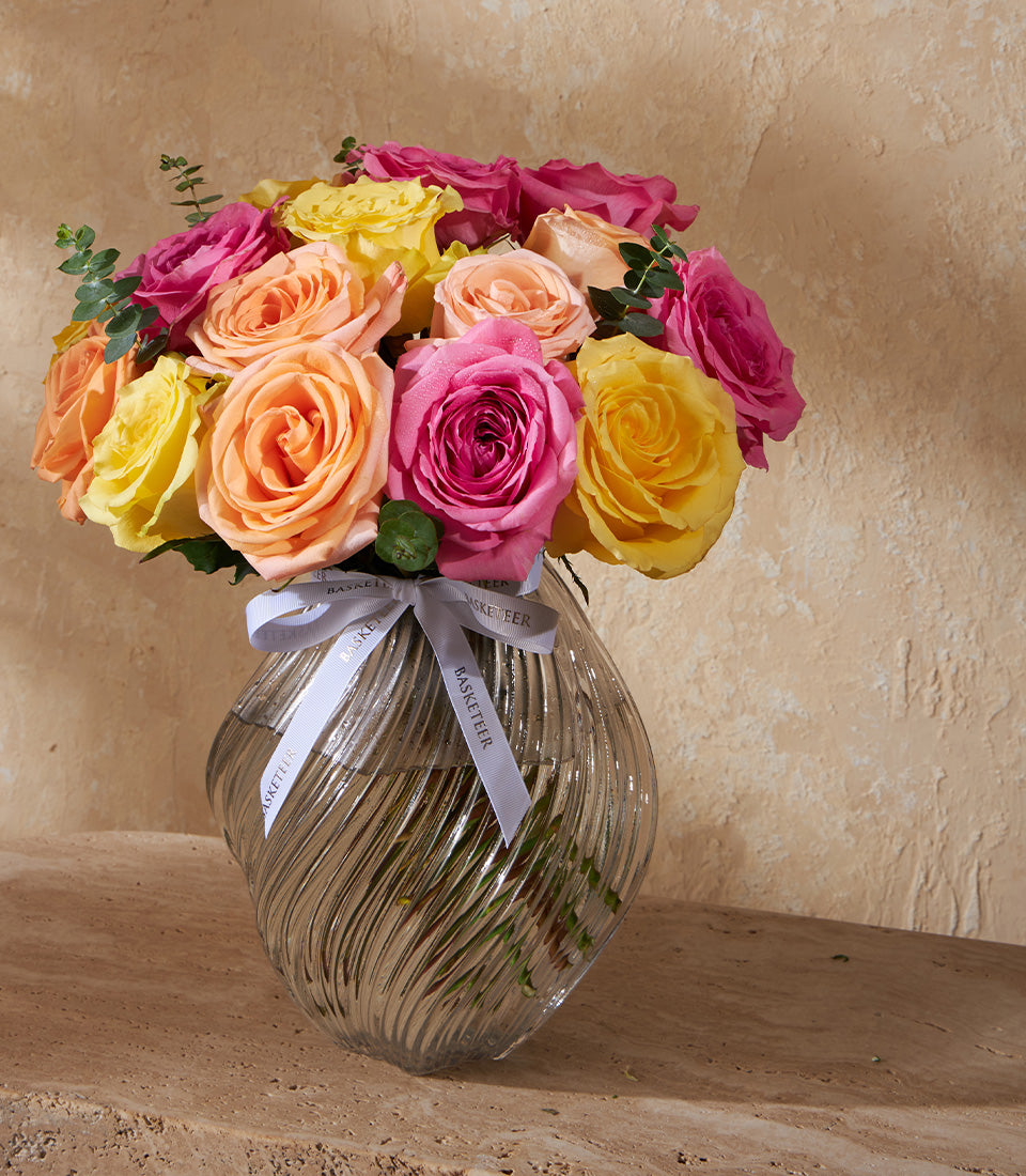 Vibrant mixed rose bouquet in textured glass vase with pink, orange, and yellow blooms