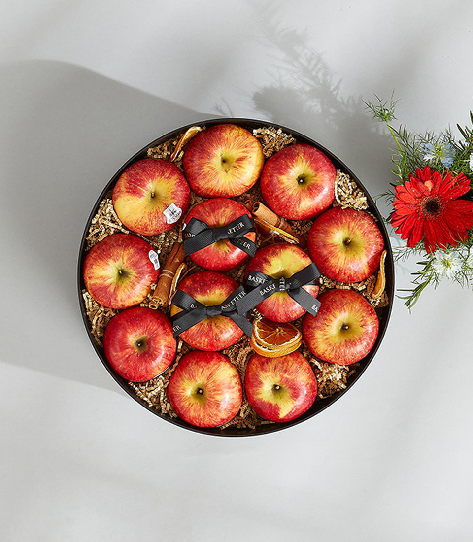 Premium red and yellow apples with cinnamon and dried citrus in black round gift box, paired with fresh red gerbera bouquet