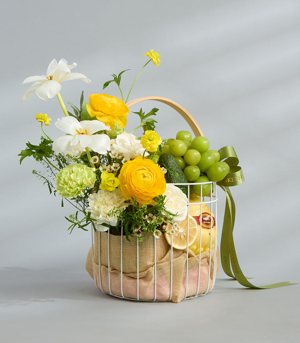 Bright yellow and white floral fruit basket with daffodils, ranunculus, fresh produce, and burlap liner
