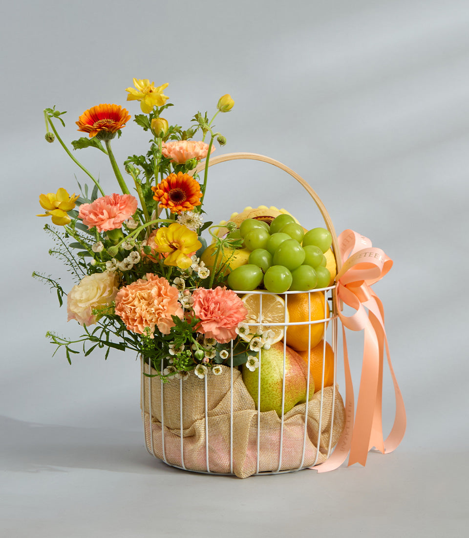 Premium fresh flowers and citrus fruits in white wire gift basket with peach ribbon