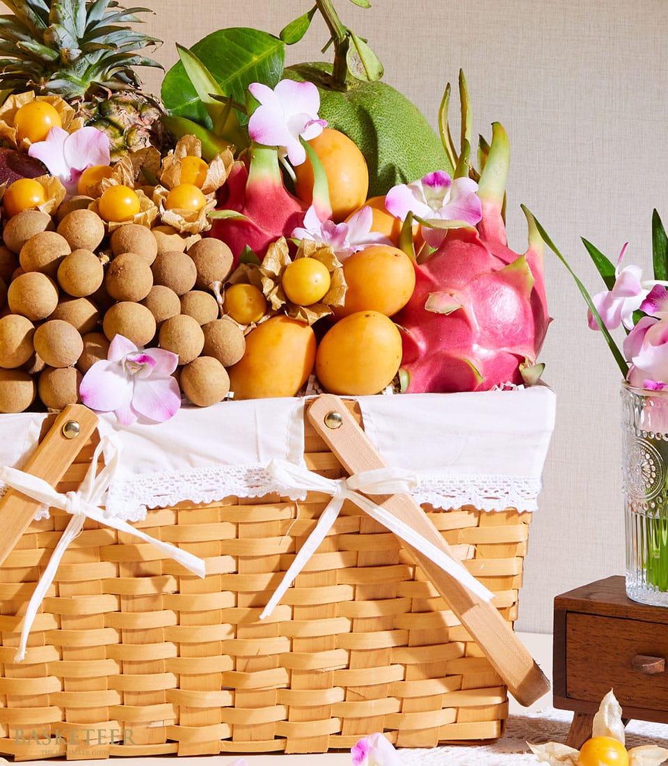 Thai tropical fruit basket with longan, mango, dragon fruit and orchids in woven wicker with pink blooms
