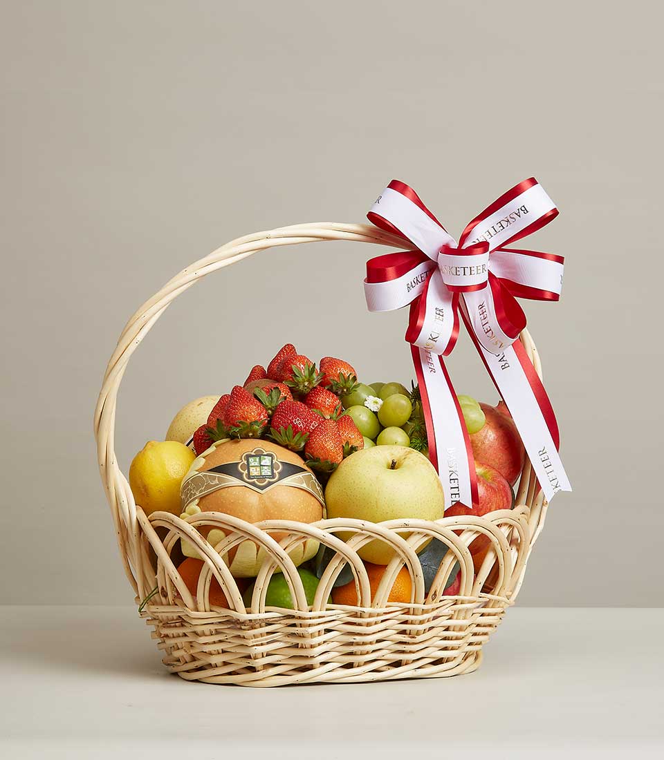 Luxury wicker fruit basket with fresh strawberries, grapes, apples, pears and lemons, tied with red and white ribbon