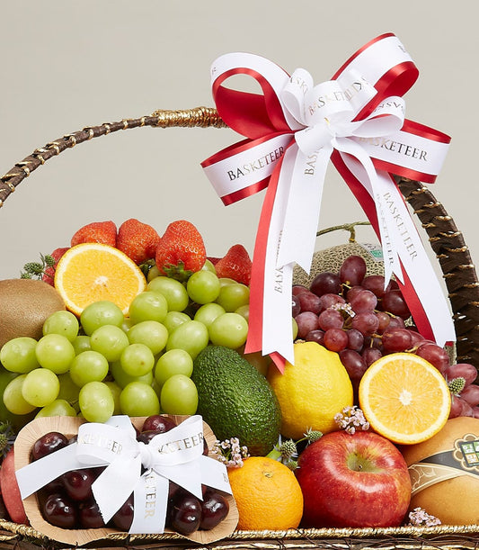 Dark woven premium fruit hamper with red ribbon bow, filled with fresh grapes, strawberries, citrus, and seasonal fruits for