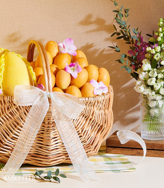 Wicker basket of Thai mango and marian plums with pink orchids and white ribbon bow