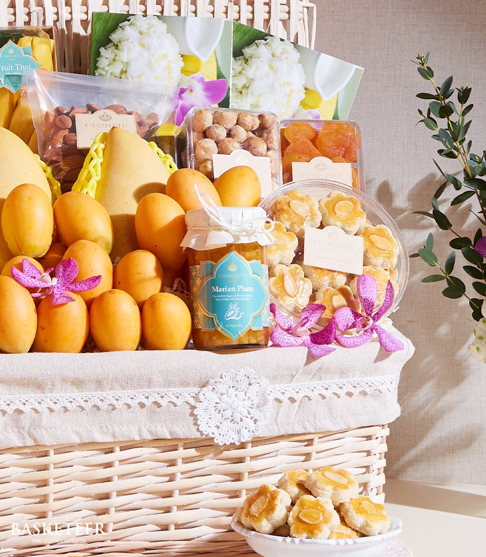 Woven wicker basket filled with fresh Thai mangoes, tropical fruits, almonds, dried apricots, cookies, and Marian plum jam,