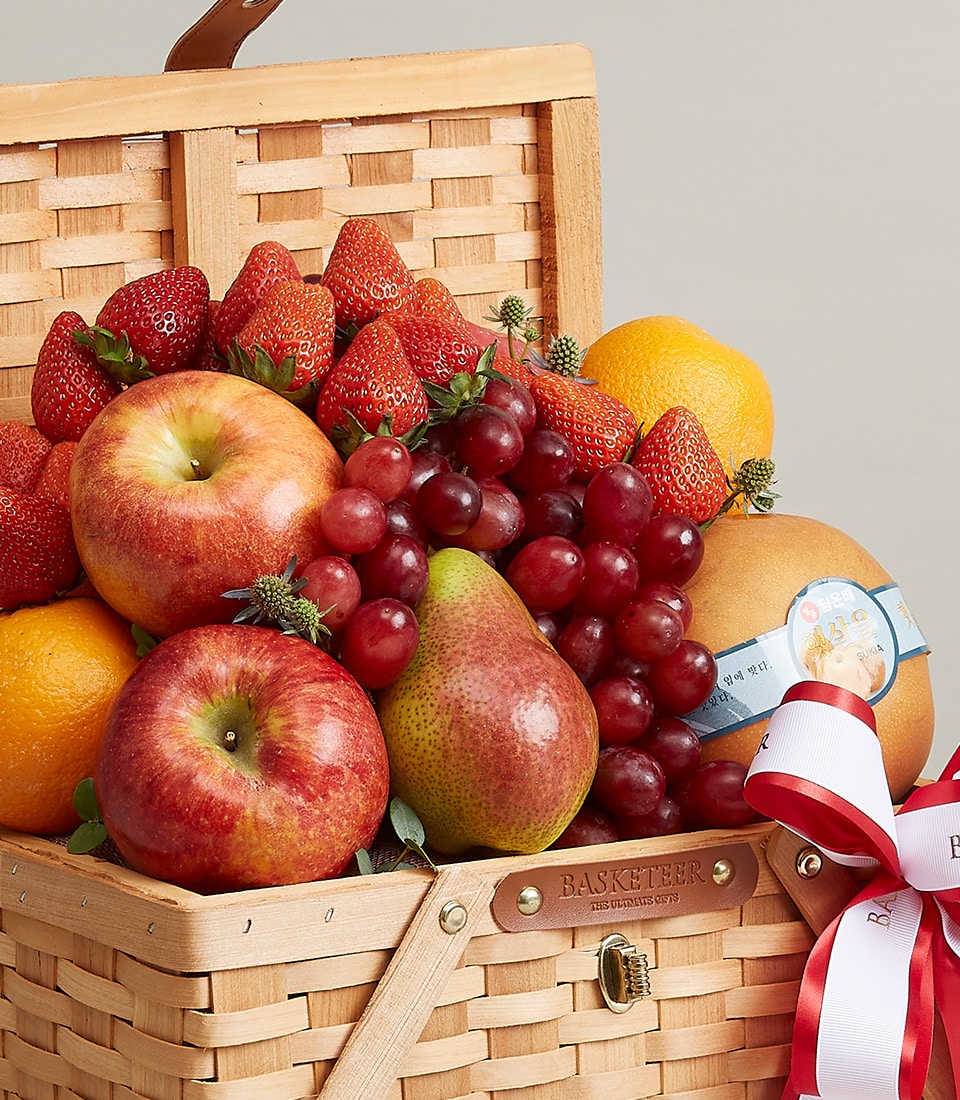 Premium woven fruit basket with fresh apples, grapes, strawberries, pears and citrus, tied with red striped ribbon for
