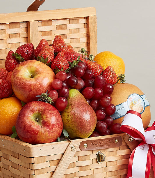 Premium woven fruit basket with fresh apples, grapes, strawberries, pears and citrus, tied with red striped ribbon for