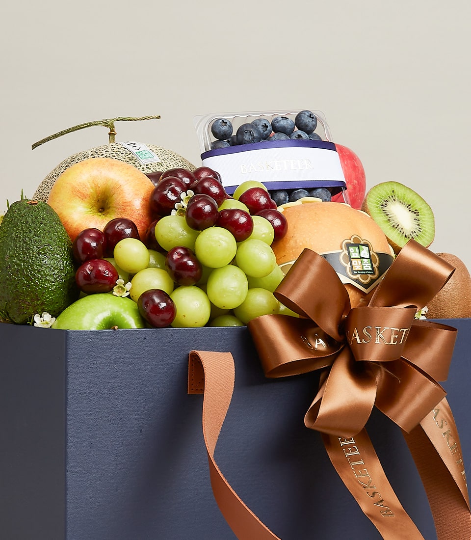 Luxury navy fruit gift bag with fresh cantaloupe, apples, avocado, grapes, cherries, blueberries and kiwi for birthday